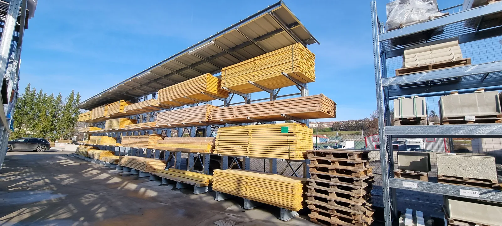 Parc de stockage extérieur Kollirama : cantilevers sous toiture chargés de bois